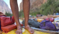 A close-up photo of a man's feet with an obvious sandle tan standing on the edge of a yellow raft.