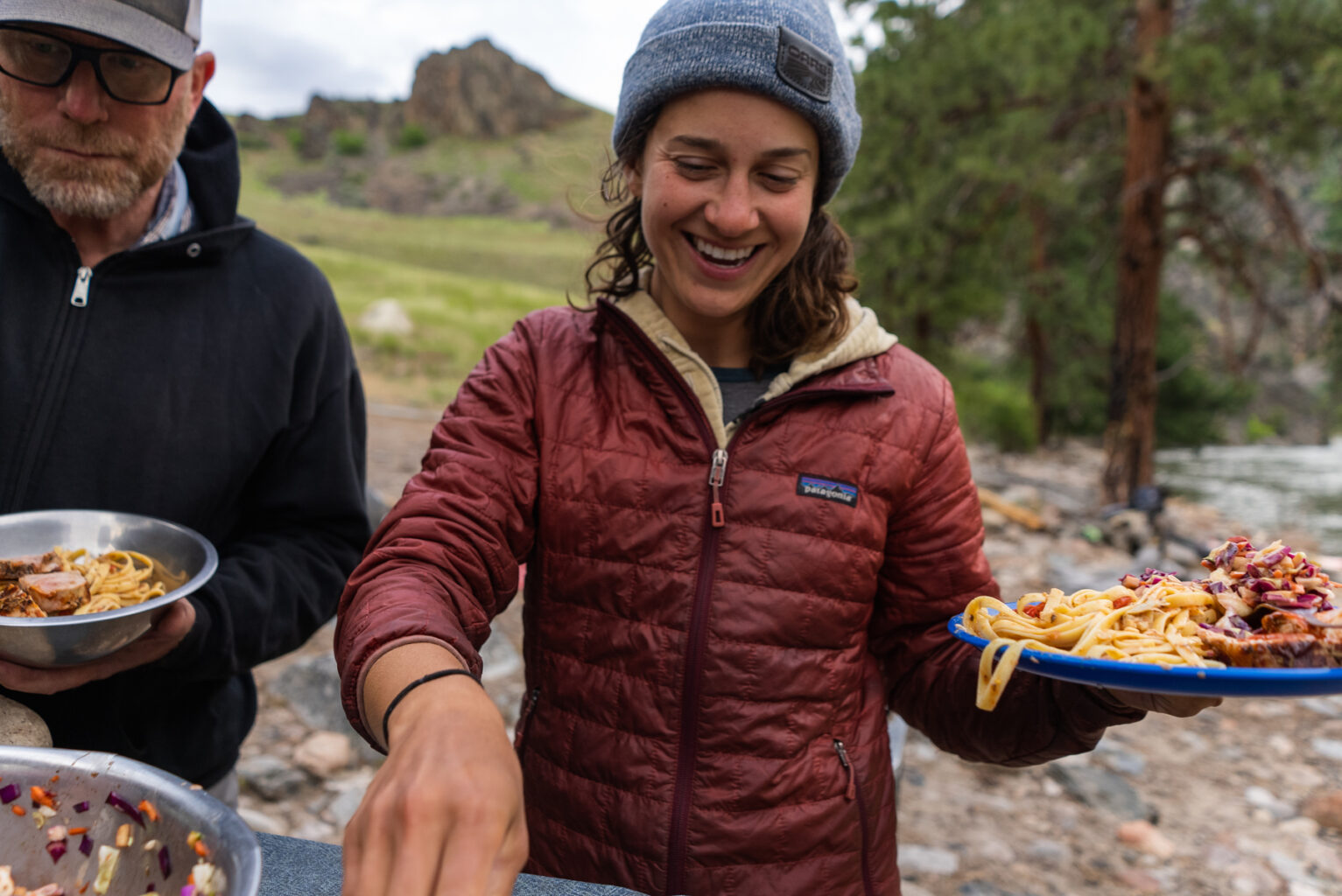 A woman in a puffy jacket serves a plate of food on a river trip with OARS in Idaho.