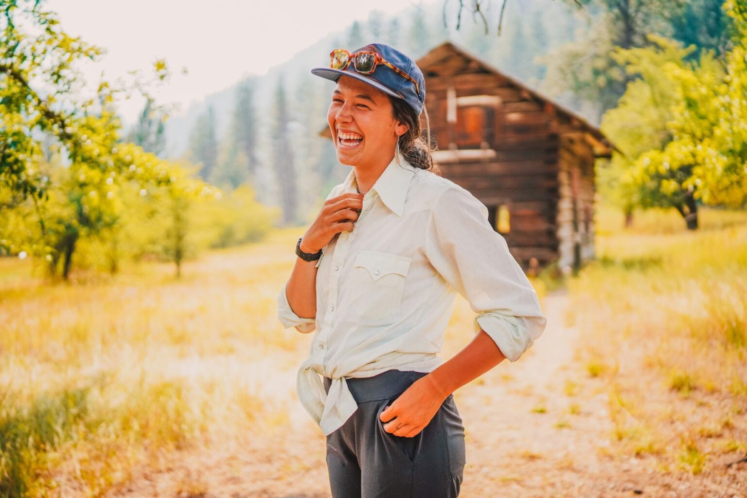 A guest on an Idaho rafting trip with OARS smiles near a historical cabin during a trip in 2024.