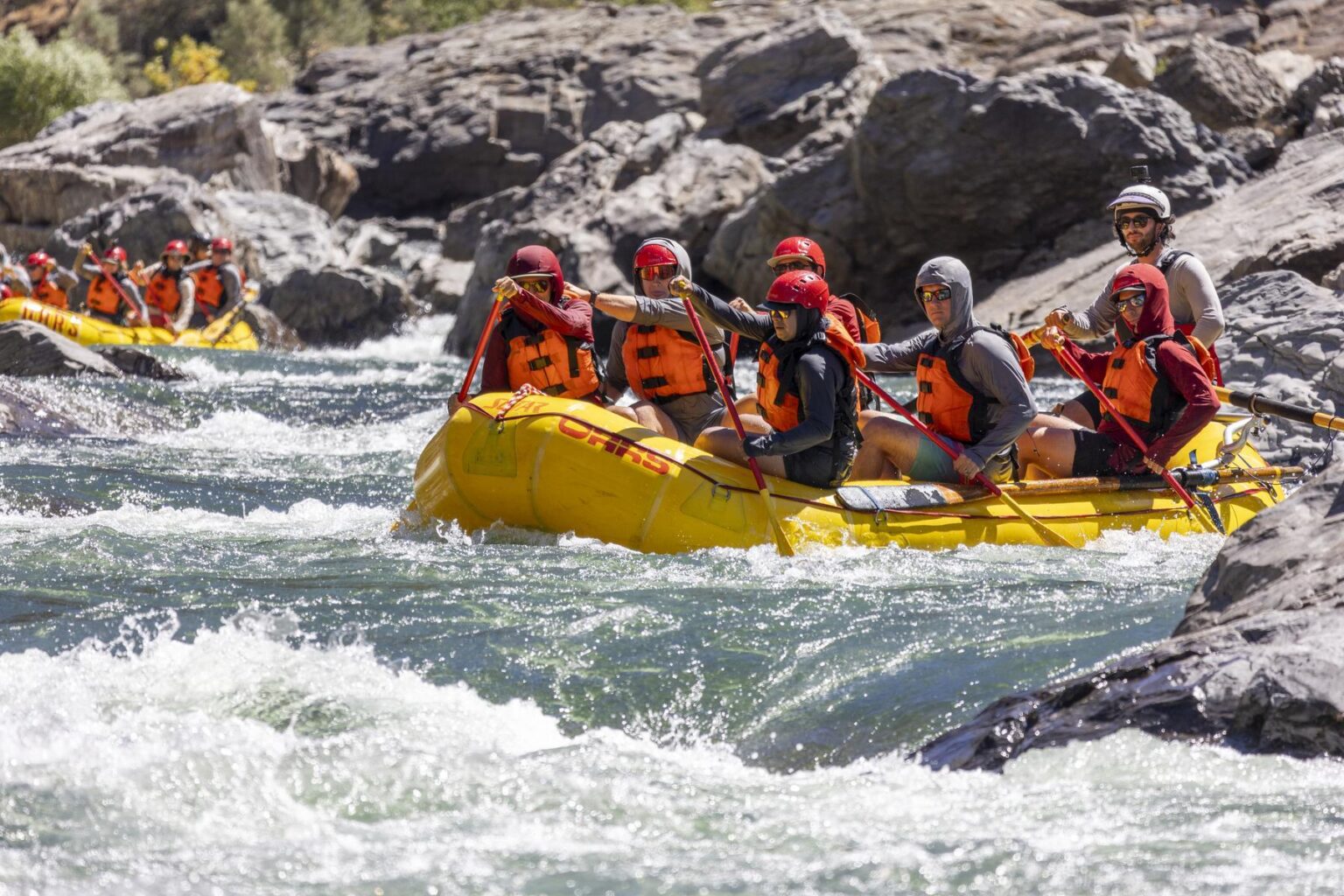 Guests on a Tuolumne River rafting trip traverse a rapid while wearing hooded sun shirts.