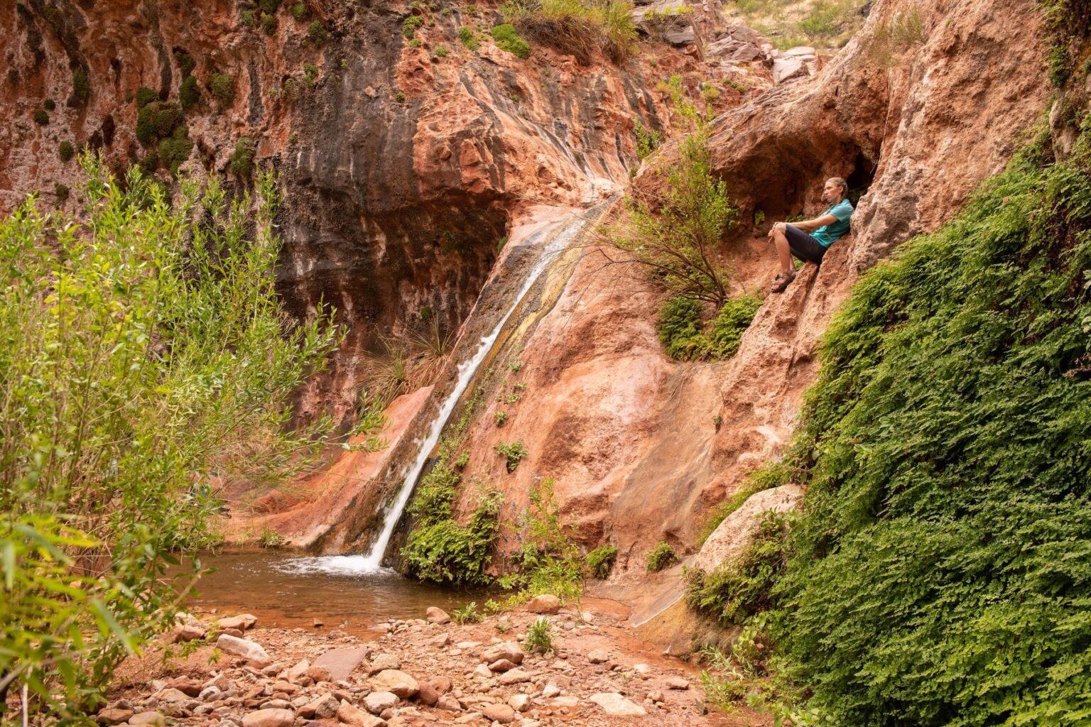 A woman rests near the waterfall at the end of the Stone Creek hike during a Grand Canyon rafting trip with OARS. 