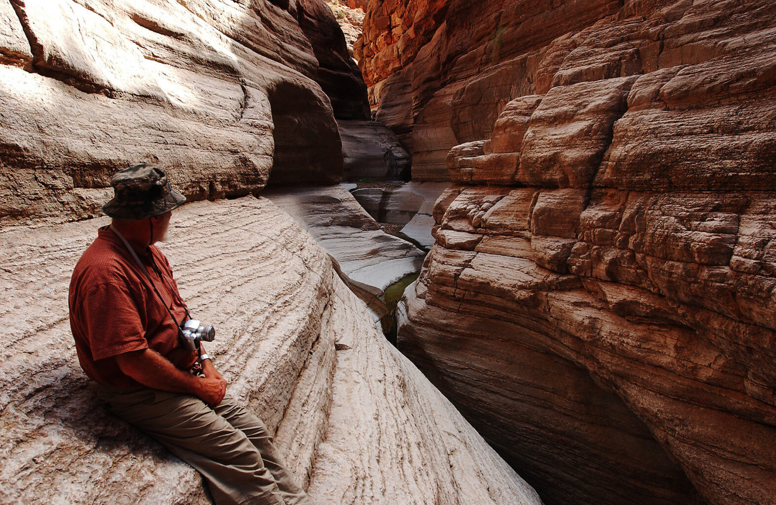 A man looks into a narrow section of National Canyon in the lower area of Grand Canyon during a hike.