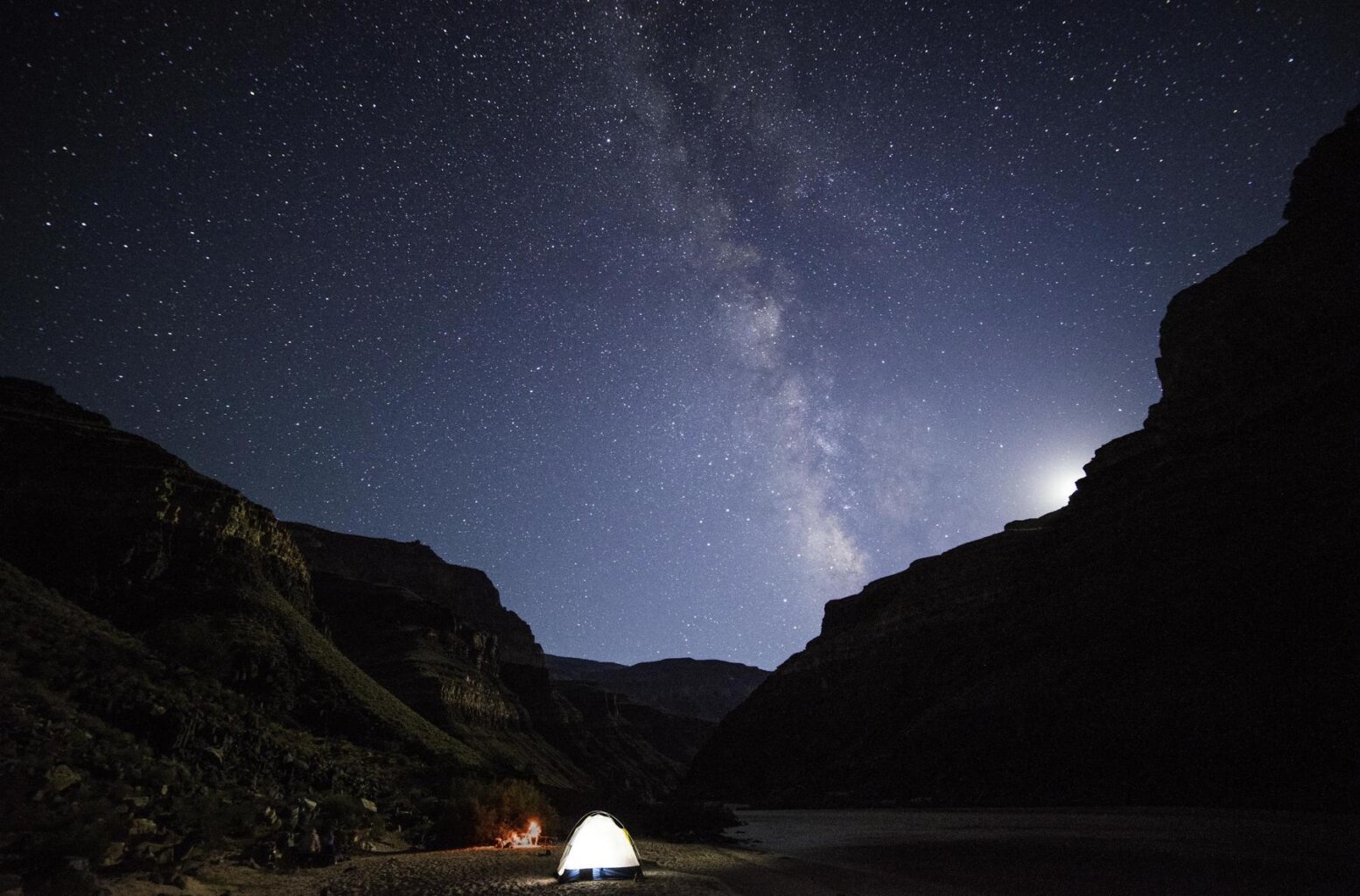 The Milky Way over Grand Canyon with a tent lit up in the foreground.