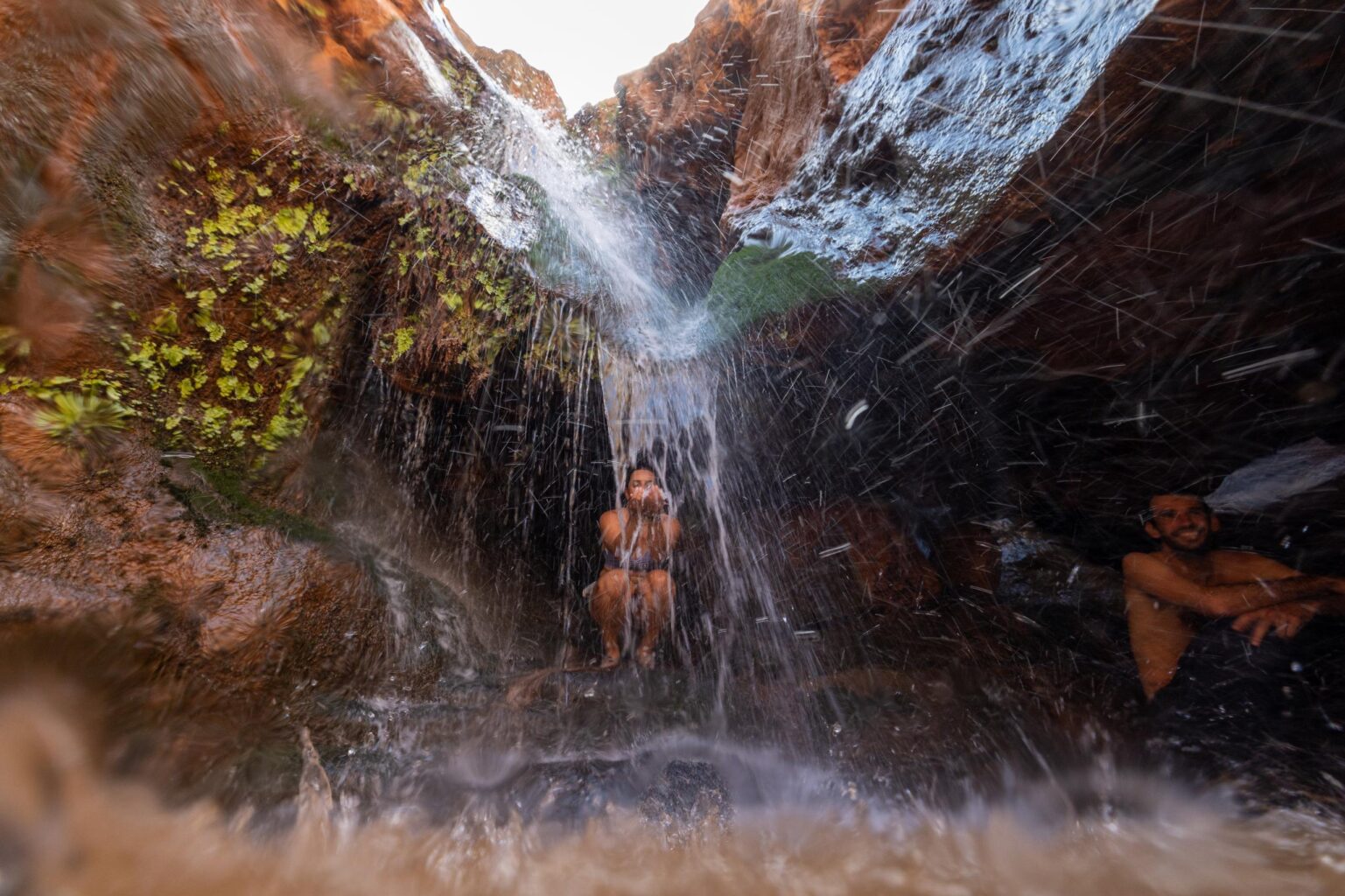 A woman reaches for dripping water in a cavern in a side canyon of Grand Canyon