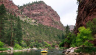 Scenic shot of yellow rafts coming down the Green River surounded by lush greenery and canyon walls