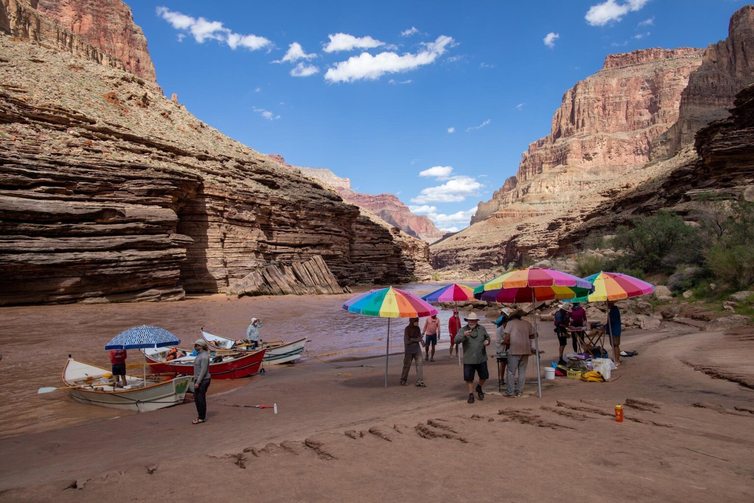 Three dories stop along the side of the river and the guests enjoy lunch under rainbow umbrellas