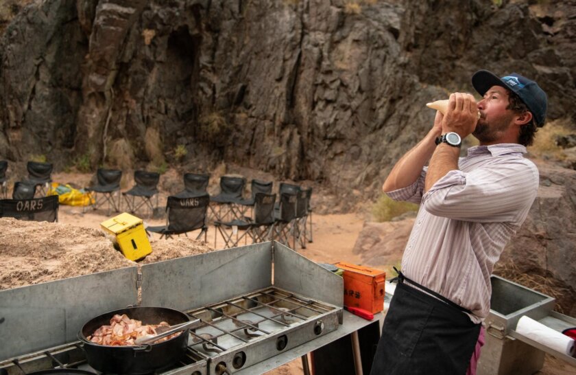 A guide blows the conch for breakfast during a Grand Canyon dory trip with OARS