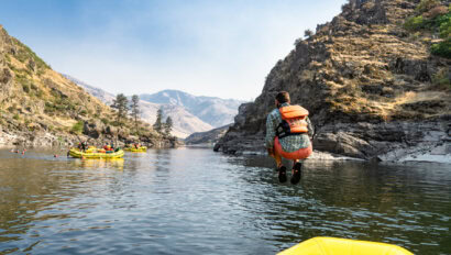 A man wearing an orange life jacket does a cannonball off of a yellow raft into a calm stretch of river