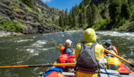 A guide rowing an oar raft down a scenic river with two guests in front as passengers
