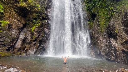 A boy stands at the base of a waterfall in Costa Rica