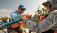 A man holding onto oars as a training guide helps adjust his technique.