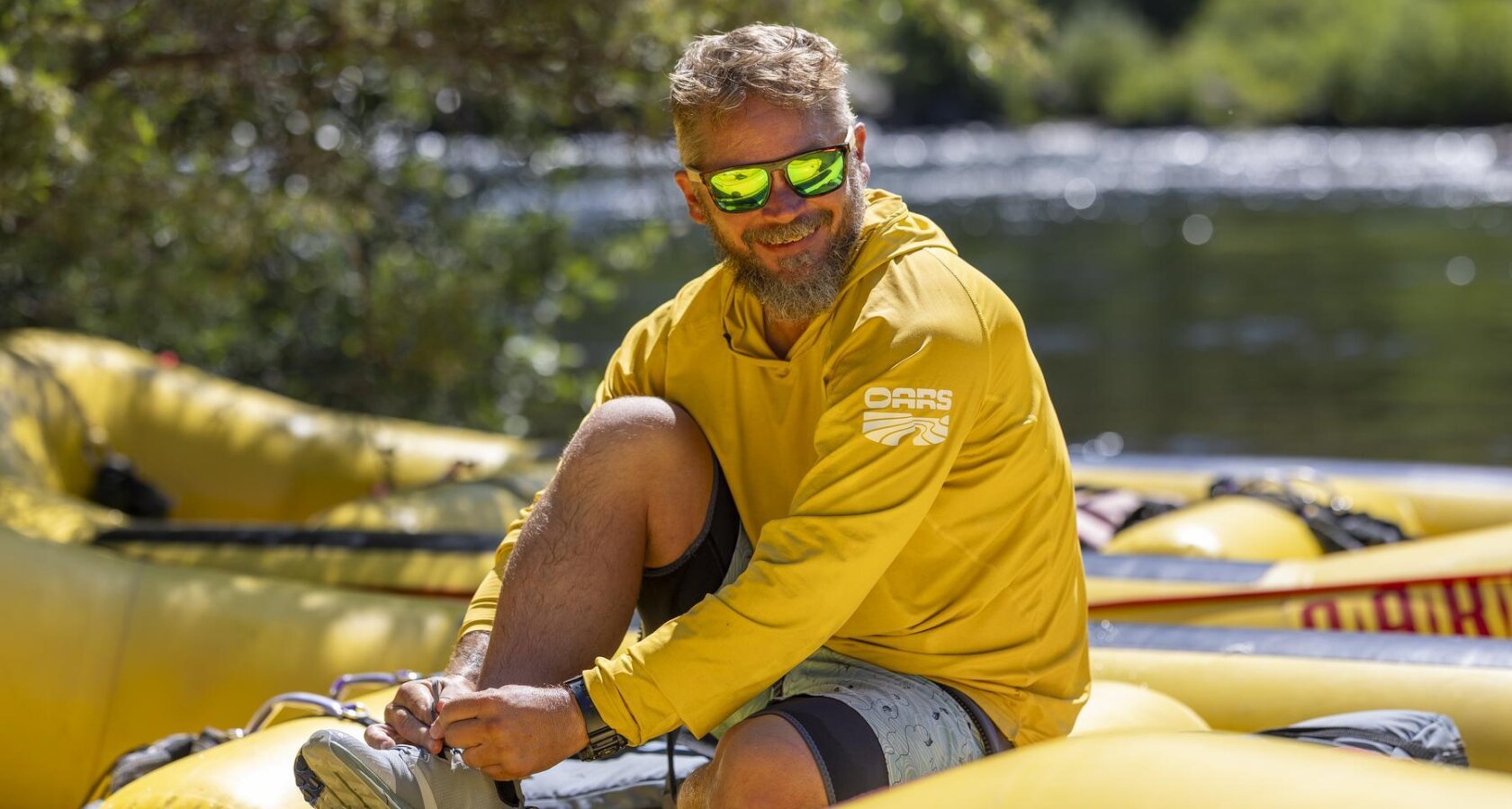 A photo of an OARS guide in a sun hoody, sitting on a raft near the American River