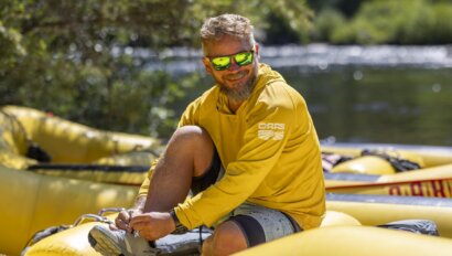 A photo of an OARS guide in a sun hoody, sitting on a raft near the American River