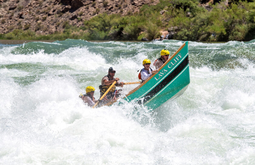 OARS dory in Lava Falls with front half of the boat right out of the water and guests hanging on for the ride