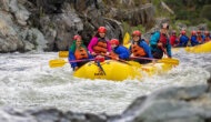 A yellow raft full of smiling paddlers makes their way downstream through a stretch of small rapids on the South Fork American River.