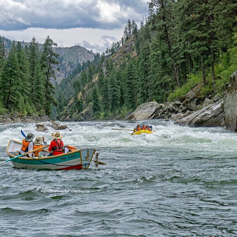 A dory full of people watches from below a rapid as an oar raft makes its way through the stretch of whitewater.