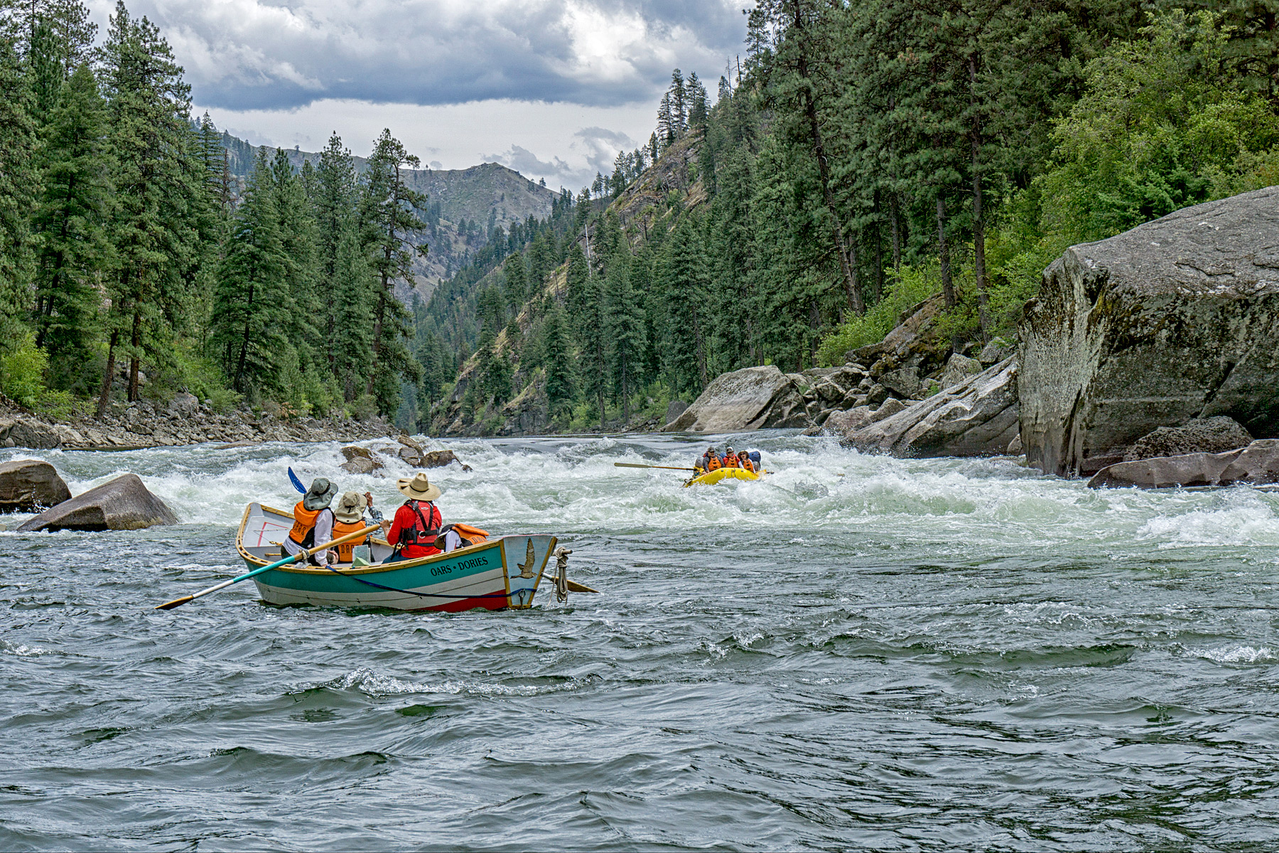A dory full of people watches from below a rapid as an oar raft makes its way through the stretch of whitewater.