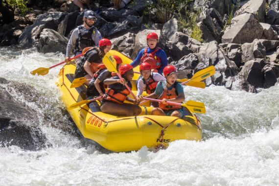A group of young people smiling while rafting through Troublemaker Rapid on the South Fork of the American River.