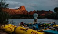 A guest stands on a raft looking over the San Juan River during sunset