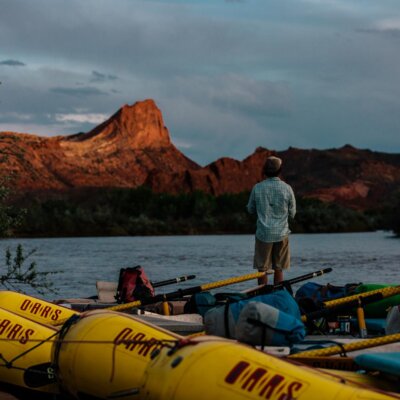 A guest stands on a raft looking over the San Juan River during sunset