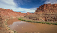 Aerial view of the Colorado River with several tiny, bright yellow rafts floating downstream