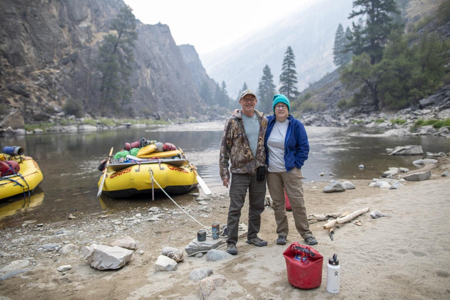 A couple poses in front of a yellow raft with their gear packed in front of them.