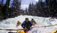 A person rows an oar raft while two passengers paddle agressively through a torrent of whitewater.