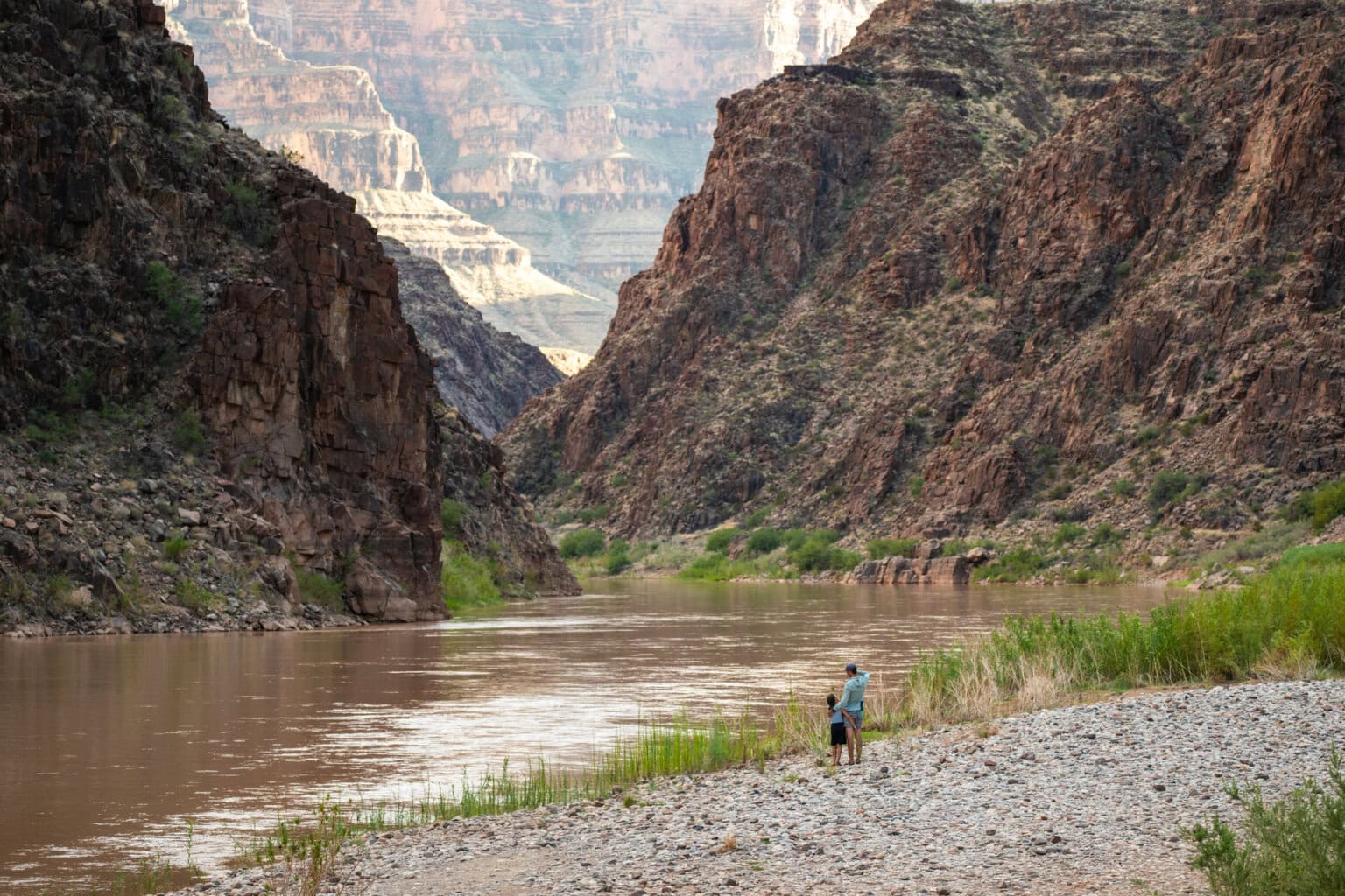 A father and child stand on the banks of the Colorado River in Grand canyon
