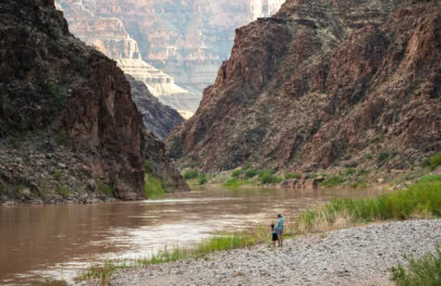 A father and child stand on the banks of the Colorado River in Grand canyon