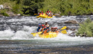 Two yellow rafts navigate through swift river rapids, surrounded by lush greenery under a bright sunny sky.