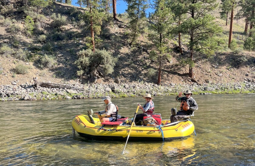 A river guide rows while two men fish from the front and rear of the raft on the scenic Middle Fork Salmon