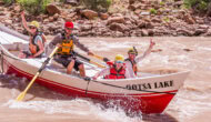 Three guests and a guide smile for the camera as they row through whitewater in a dory on the Colorado River through Cataract Canyon.