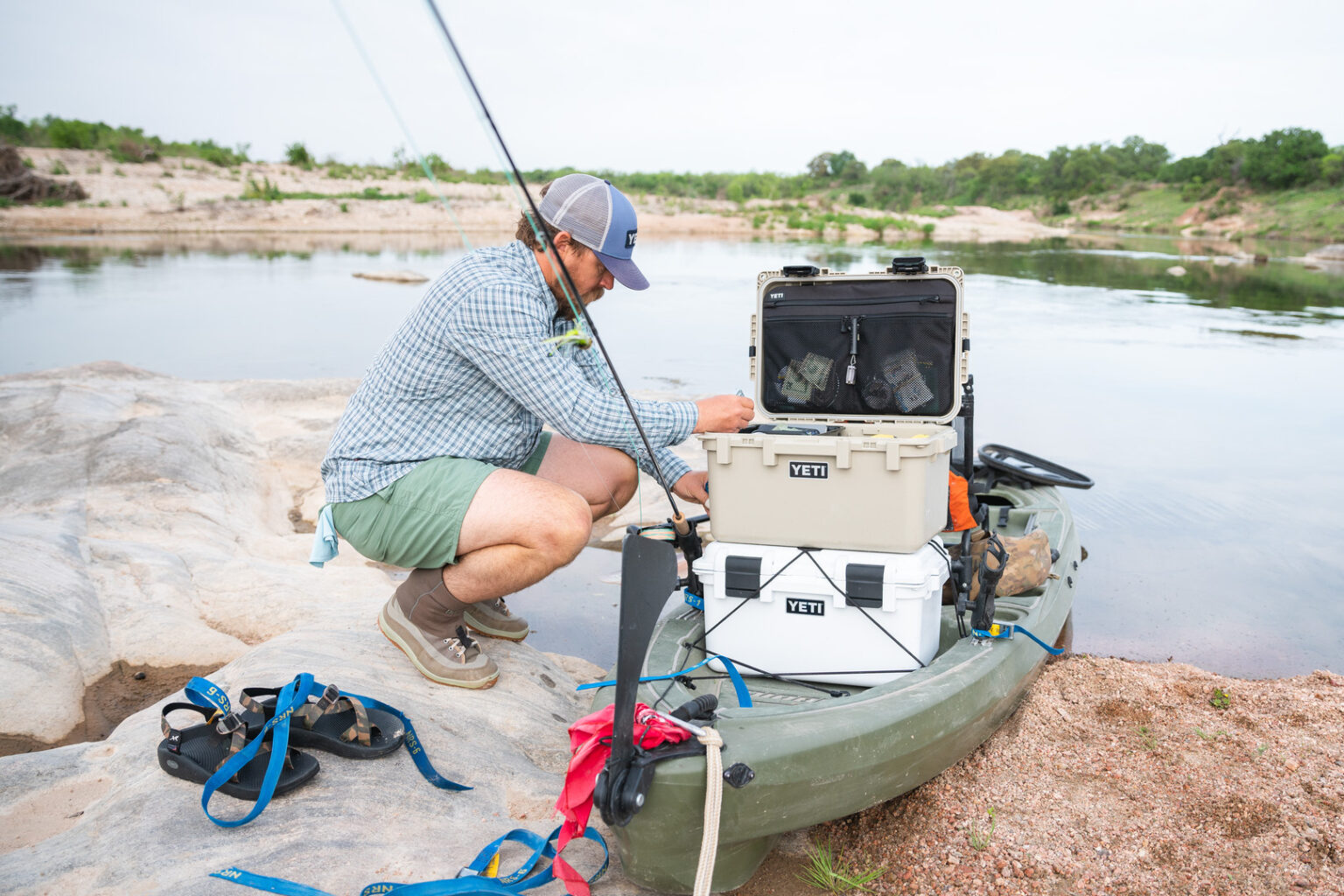 A man preps his kayak with fishing gear and heavy duty waterproof gear boxes made by YETI along the shore of a peaceful lake
