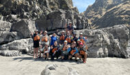 A group of people posing together outdoors in front of a rocky cliff under a clear blue sky.