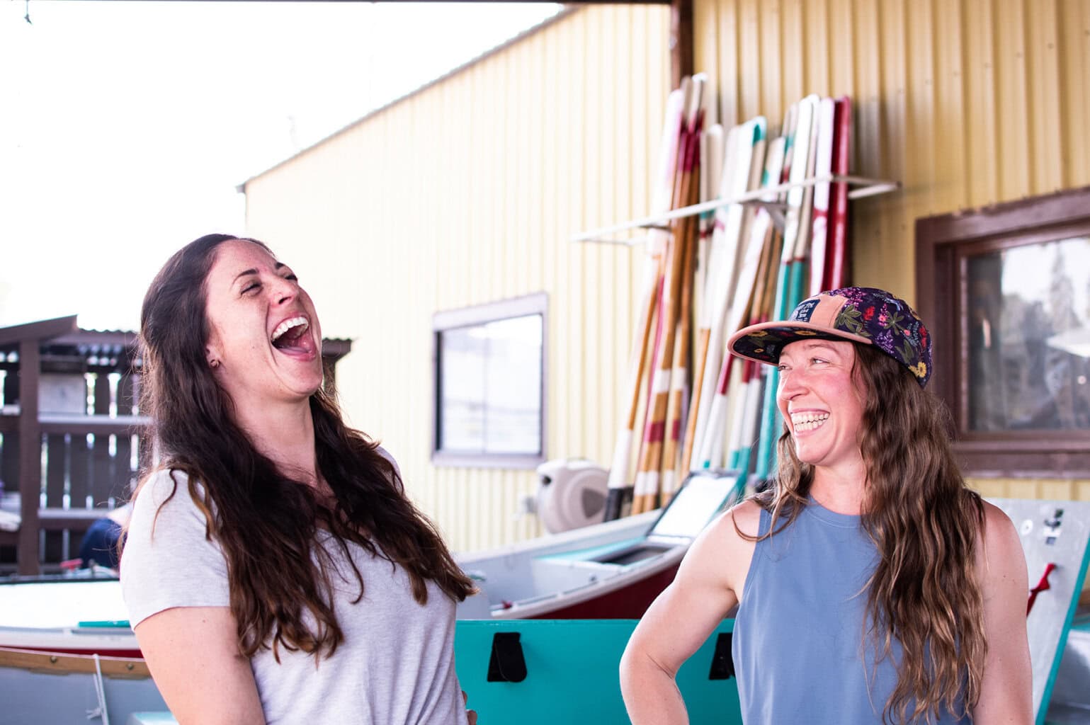 Two women laughing in an airy boathouse setting