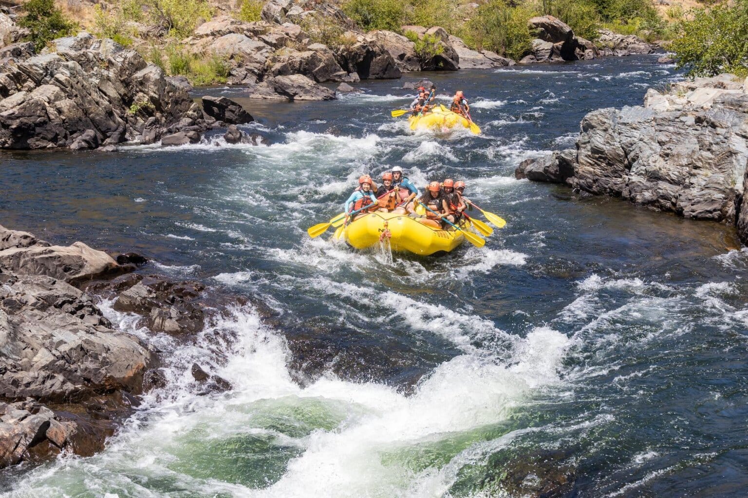 Two yellow rafts with a group of paddlers float toward whitewater riffles on the South Fork of the American River