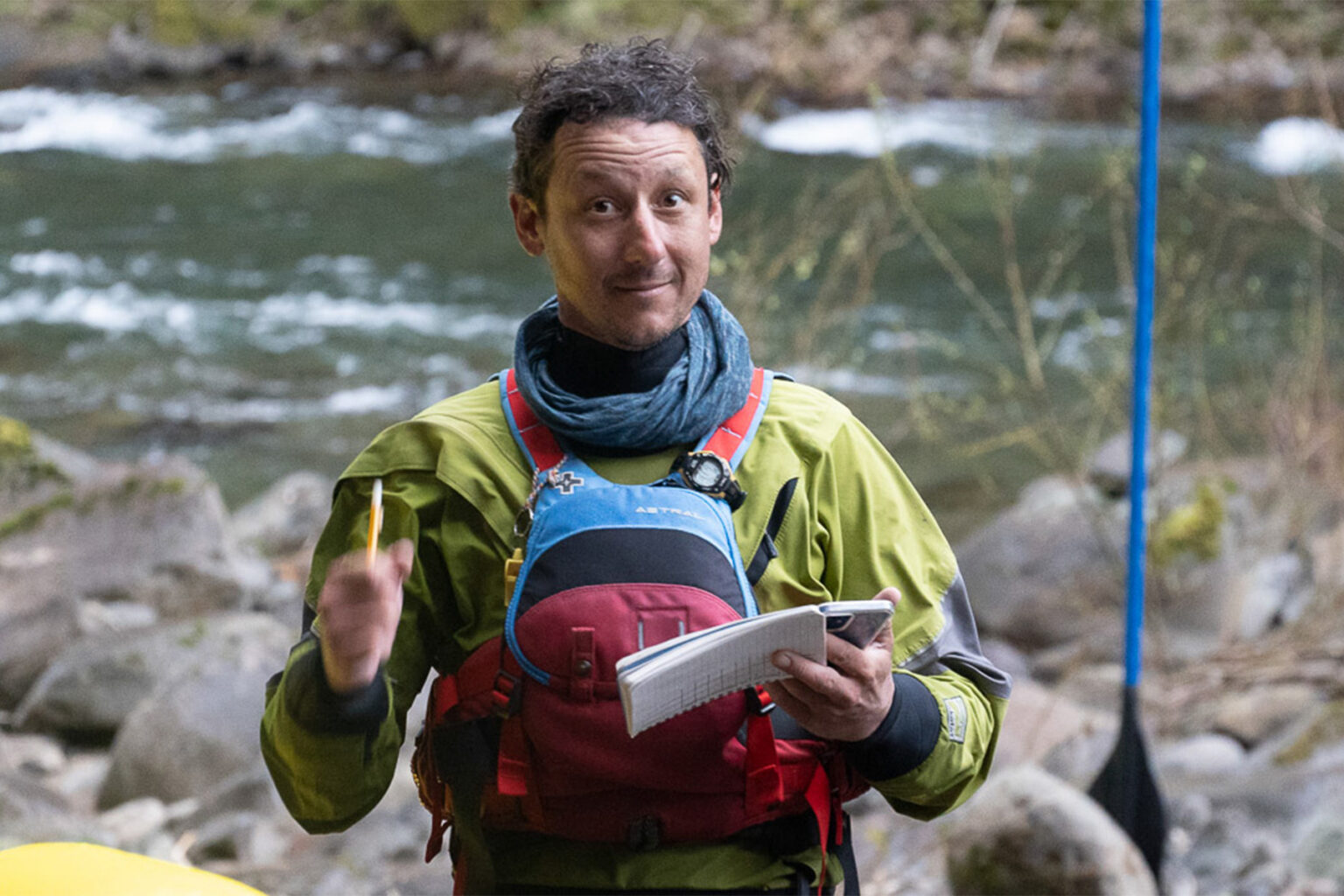 A river guide wearing a PFD standing alongside the Rogue River.