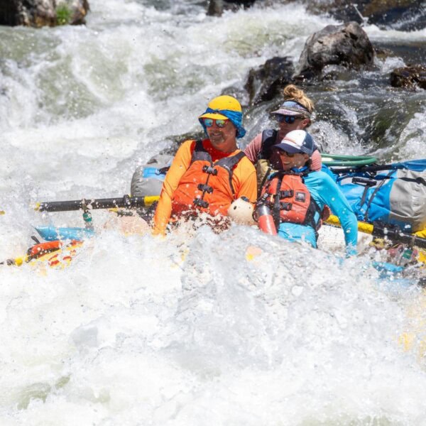 A couple sitting in the front of a yellow raft gets doused by whitewater on Oregon's Rogue River
