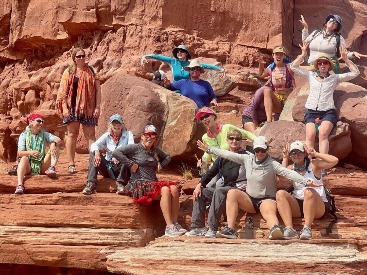 A group of women smile and make silly faces surrounded by striking redrock.