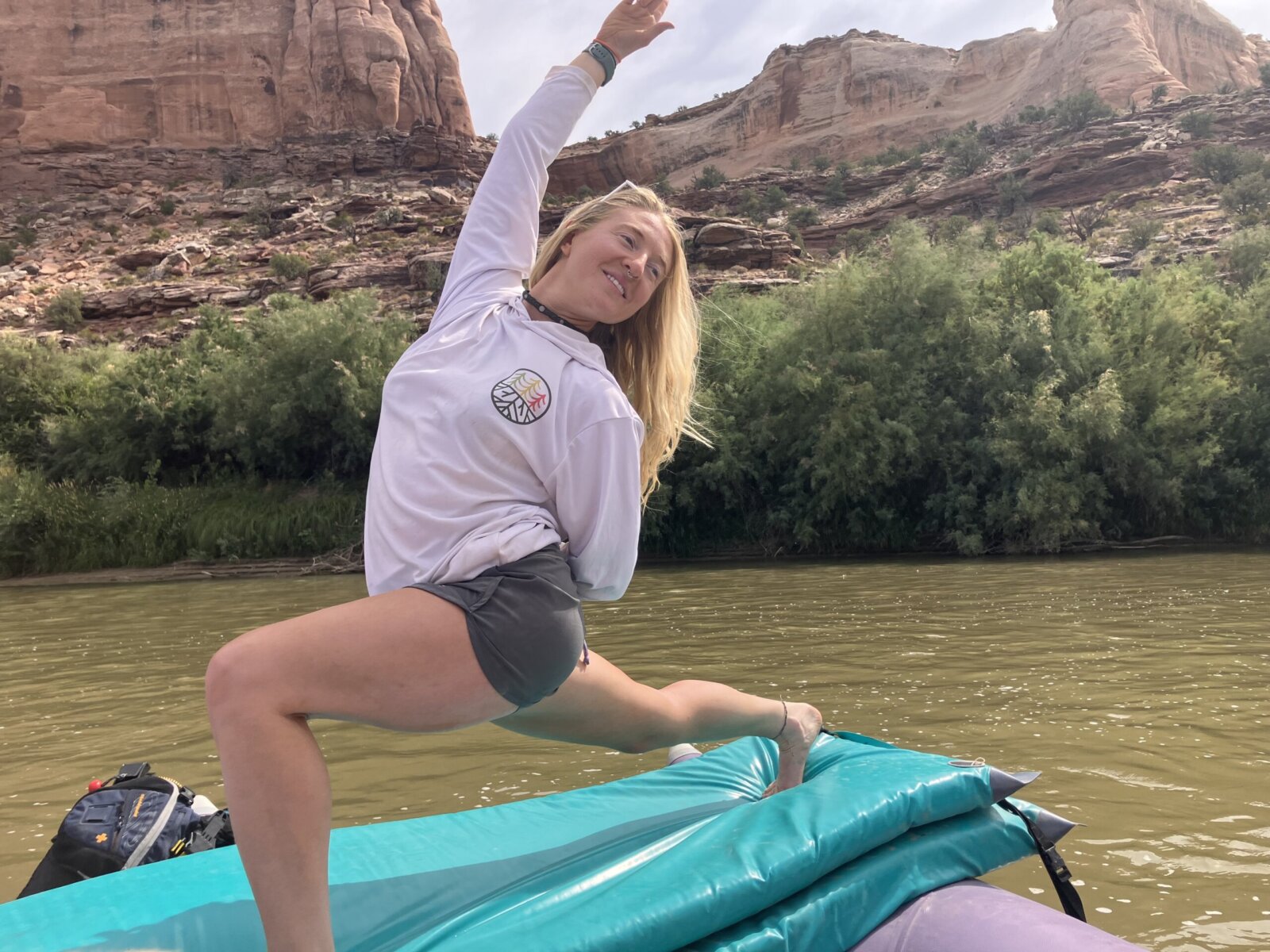 A woman strikes a yoga pose on stacked sleeping pads on top of a raft on the river.
