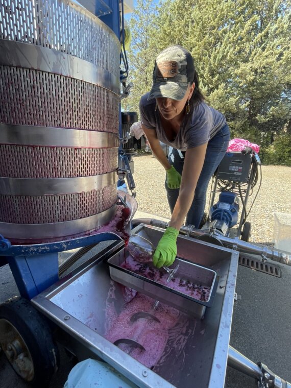 Winemaker Kate MacDonald near a piece of winemaking equipment where freshly pressed wine is flowing into a wine glass