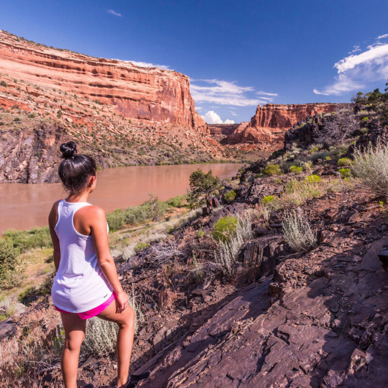 A woman stands above the Colorado River in Westwater Canyon looking out at the striking geology of black Vishnu Schist and redrock canyon walls.