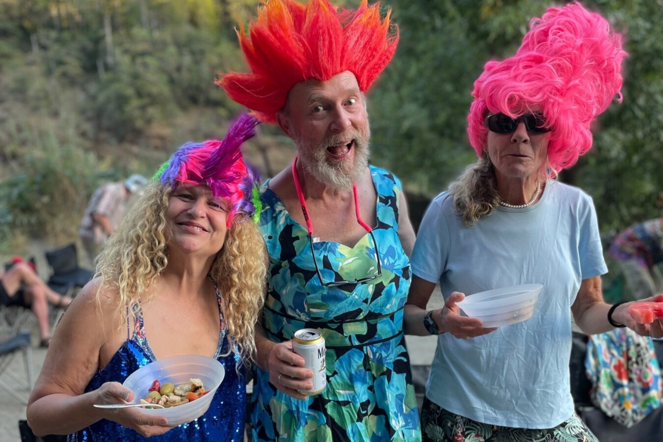 Three people in vibrant and silly costumes smile for the camera while at camp on an OARS river trip.