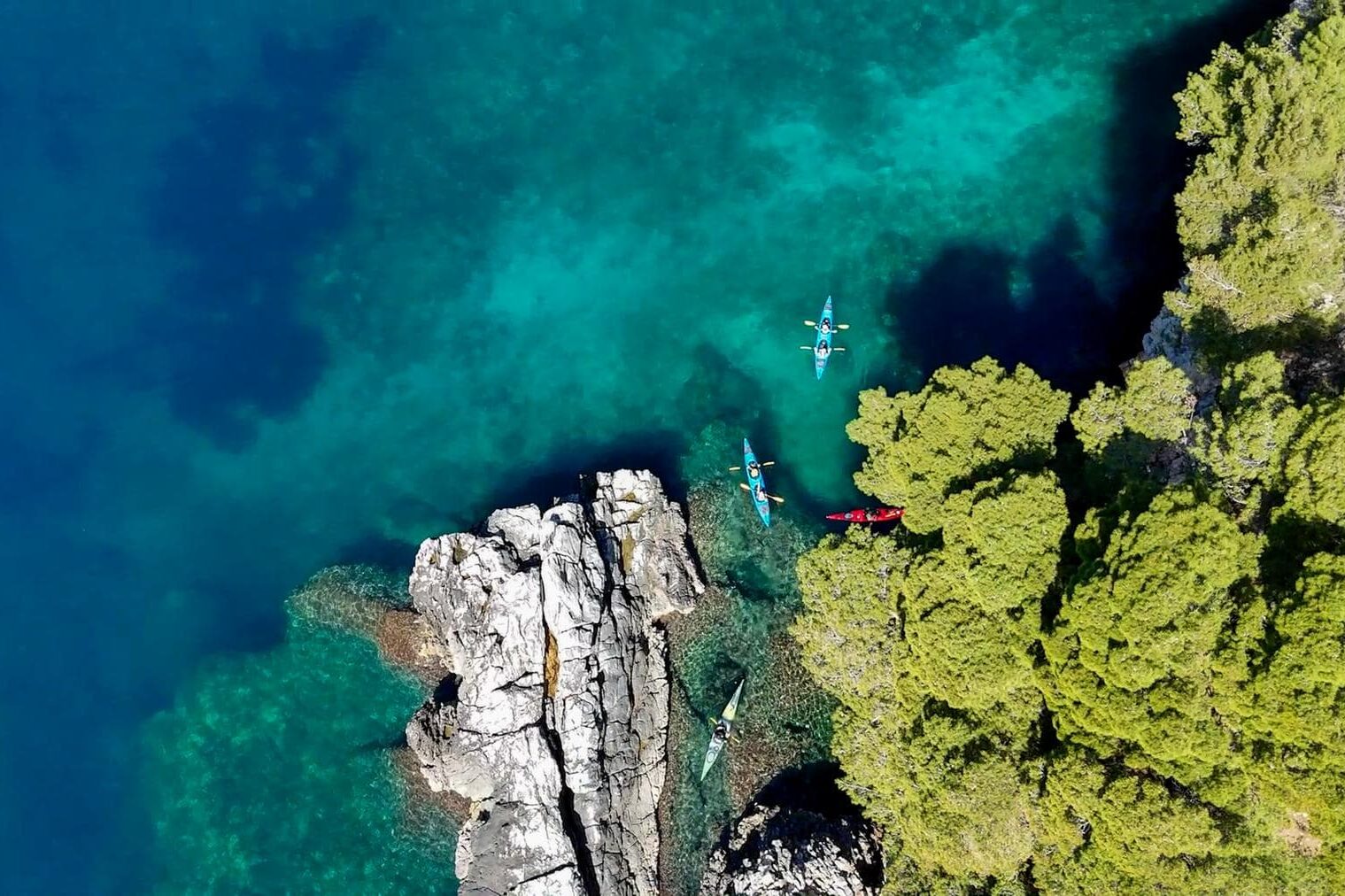 A group of kayakers paddling a craggy shoreline along the Dalmation Coast in Croatia, one of the top sea kayaking destinations in the world.