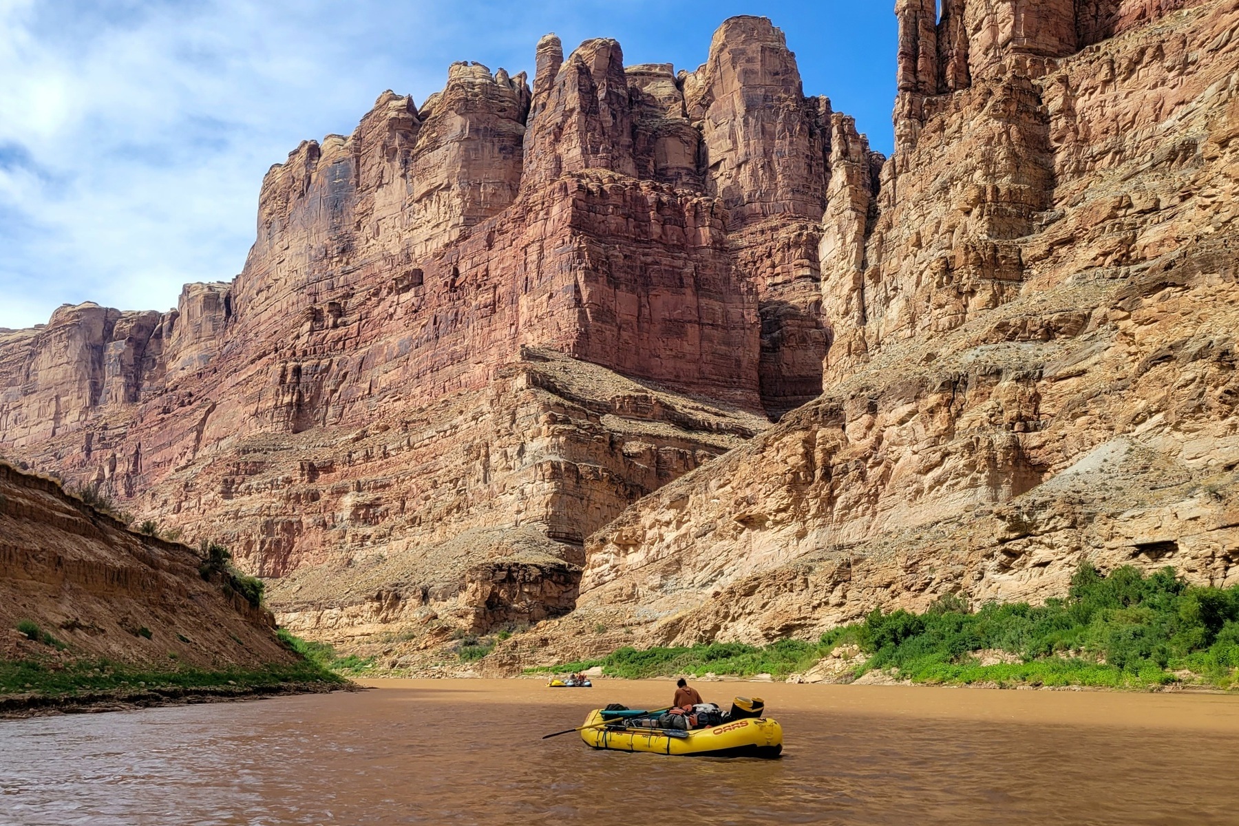 Two yellow rafts row down the Colorado River with towering canyon walls around them.