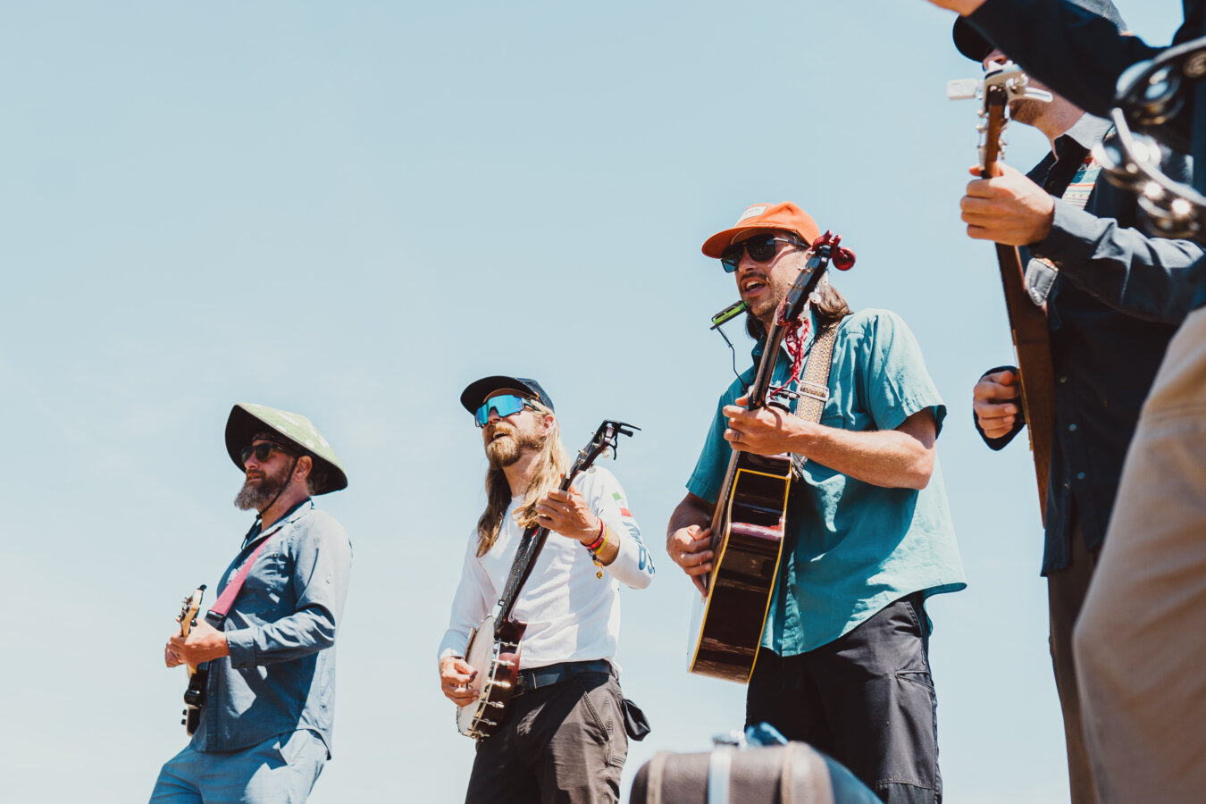 Members of A Brother's Fountain playing instruments against a bright blue sky.