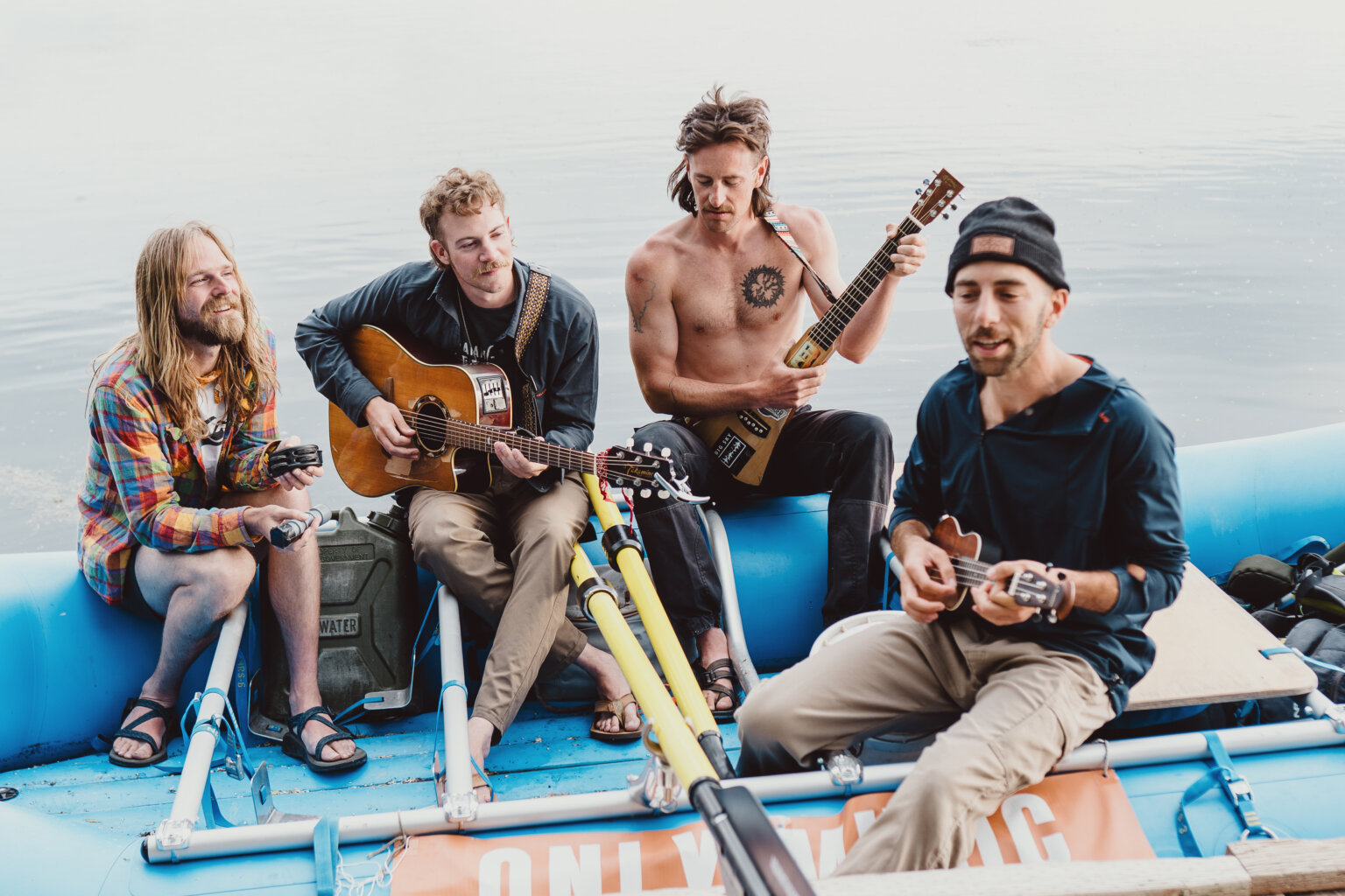 Members of A Brother's Fountain sit on a blue raft on the river and play their instruments.