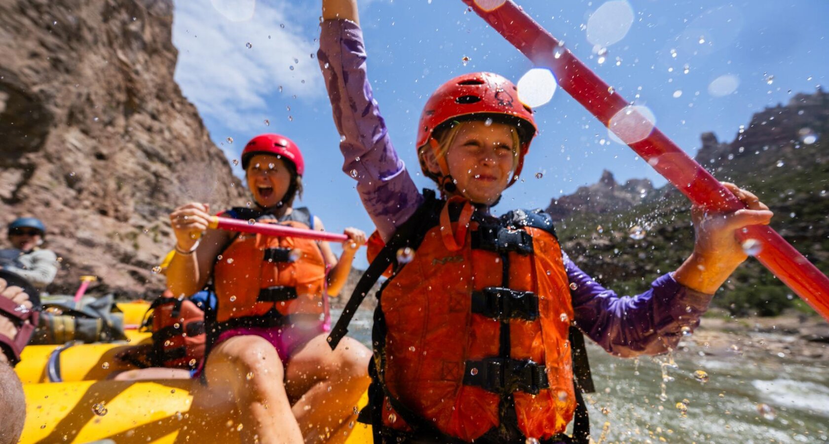A girl and her mom bing splashed by water as they paddle on a yellow raft