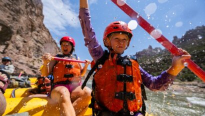 A girl and her mom bing splashed by water as they paddle on a yellow raft